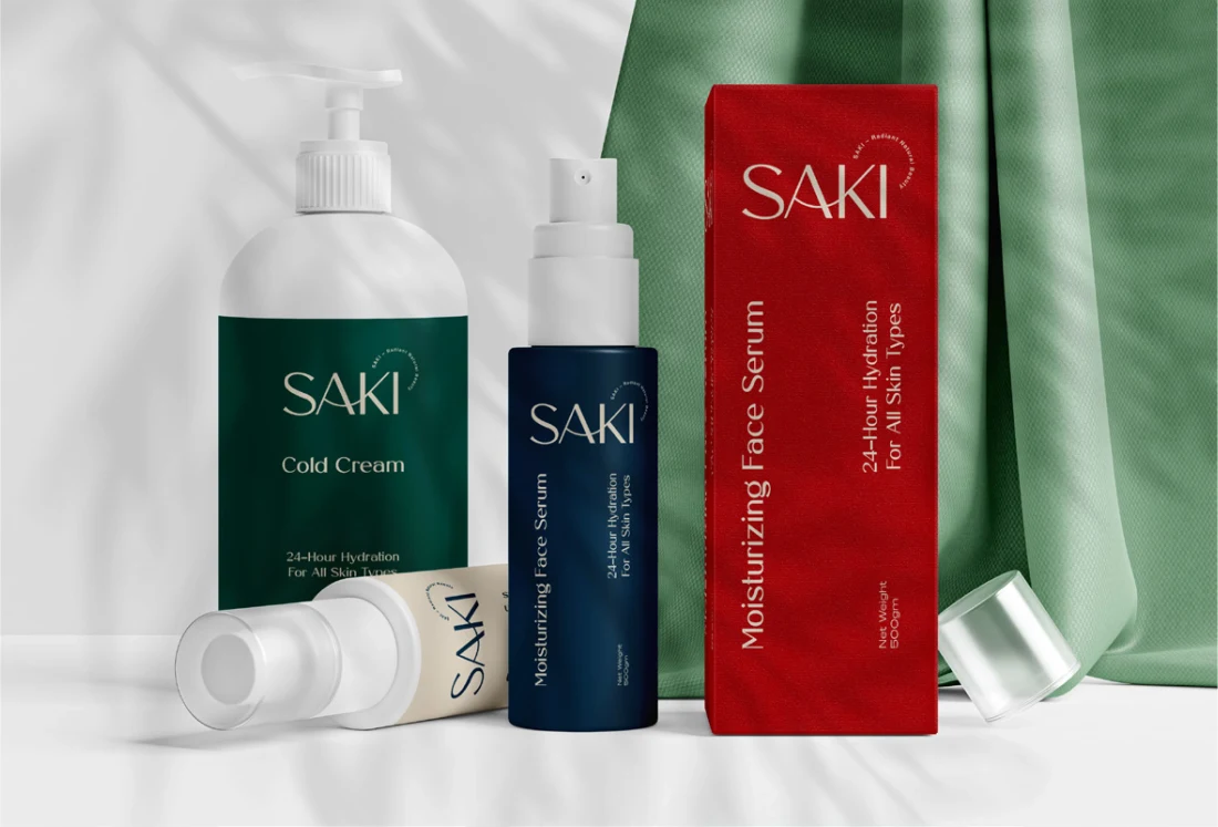SAKI skincare bottles, tubes and red packaging arranged on white fabric.